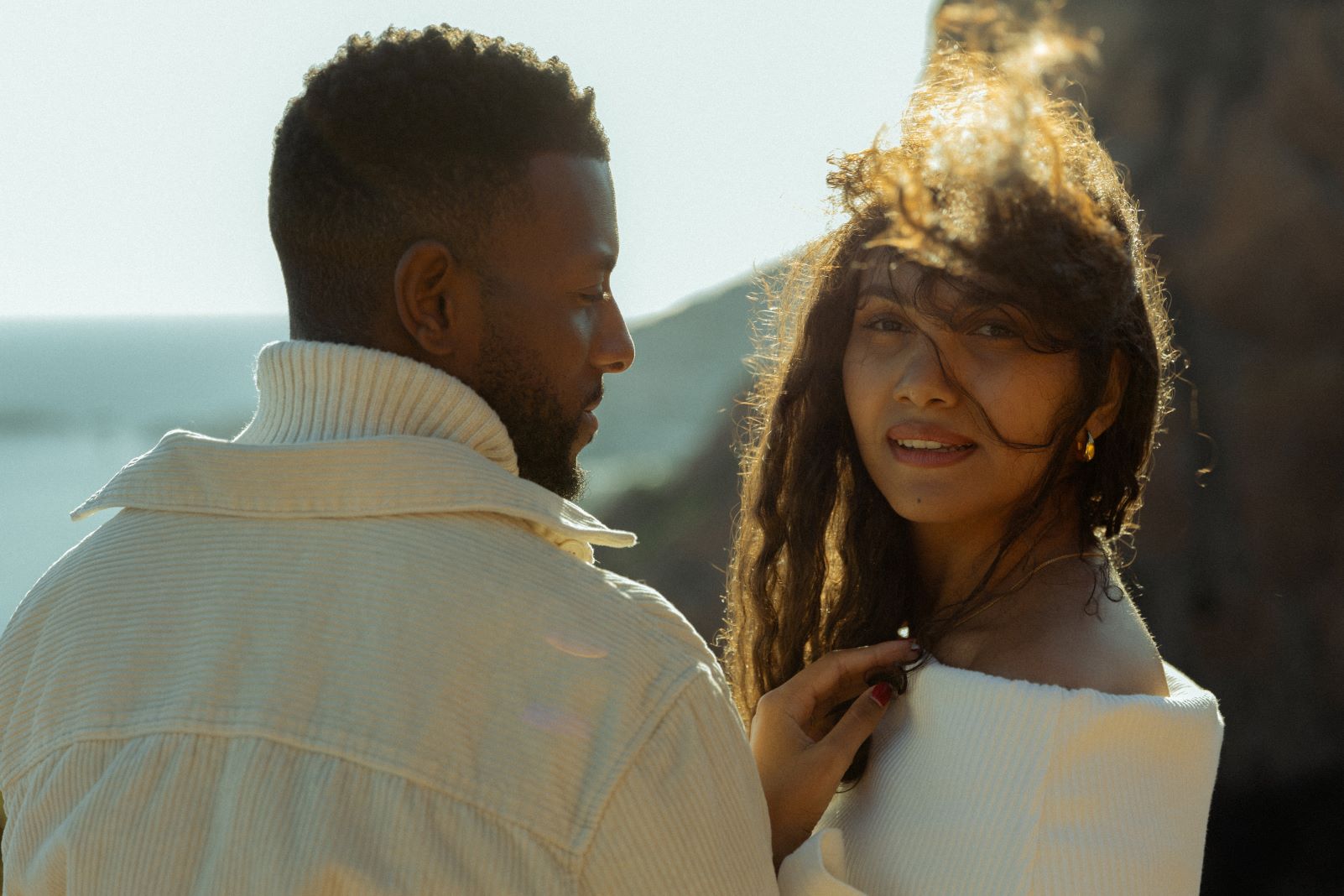 Photo d'un couple où l'homme regarde la femme et la femme regarde l'objectif, les cheveux au vent